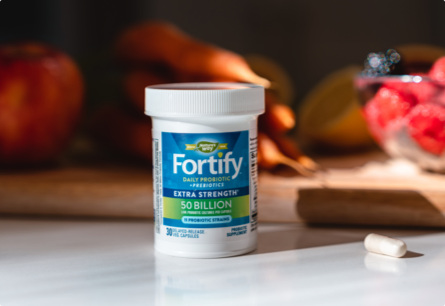 A bottle of Fortify Extra Strength Probiotics sitting on a counter with fruits and vegetables in the background.