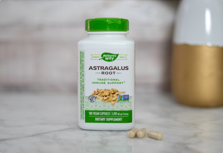 <{%DETAIL1_10180%}>A bottle of Astragalus Root sitting on a marble countertop next to three capsules.