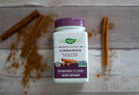 A bottle of Cinnamon capsules laying on a table between loose cinnamon powder and cinnamon sticks.