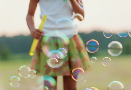 A girl blowing bubbles outside.