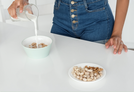 A hand pouring milk into a bowl of cereal.