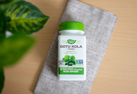 <{%DETAIL1_14000%}>A bottle of Gotu Kola Herb laying on a towel next to a leafy plant.