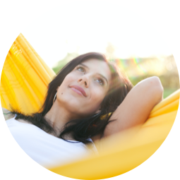 <{%ATTRIBUTE1_16000%}>A woman laying in a yellow hammock and looking at the sky.