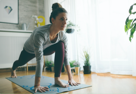 A woman in a bright room doing yoga with plants in the background.