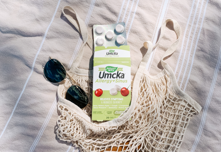 A packagle of Umcka Allergy and Sinus laying next to a handbag and a pair of sunglasses.