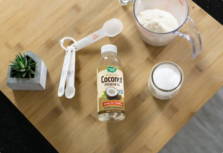 A bottle of Coconut Oil laying on a countertop next to measuring spoons and a measuring cup.