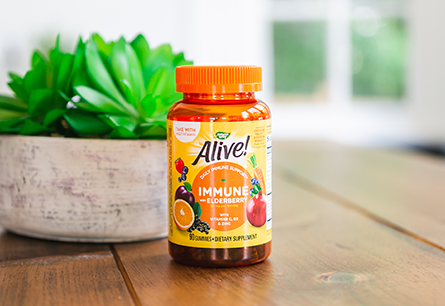 <{%DETAIL1_10484%}>One bottle of Alive Immune Gummies on wood dining table.