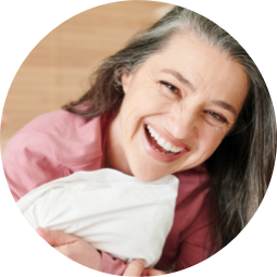 <{%ATTRIBUTE1_07480%}>A woman smiling and hugging a pillow.