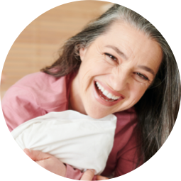 A woman smiling and hugging a pillow.