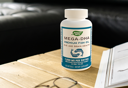 A container of Nature's Way Mega DHA premium fish oil on a table next to a book and a pair of glasses.