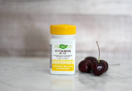 A bottle of Vitamin B-12 sitting on a table next to cherries.